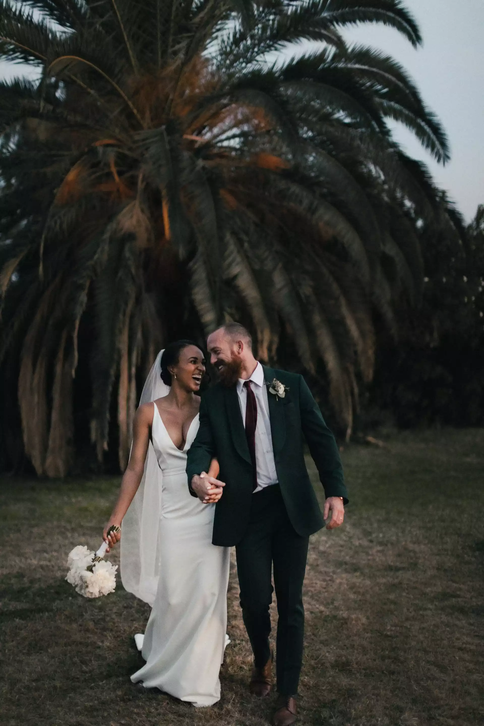 un couple de mariés souriant devant un arbre tropical