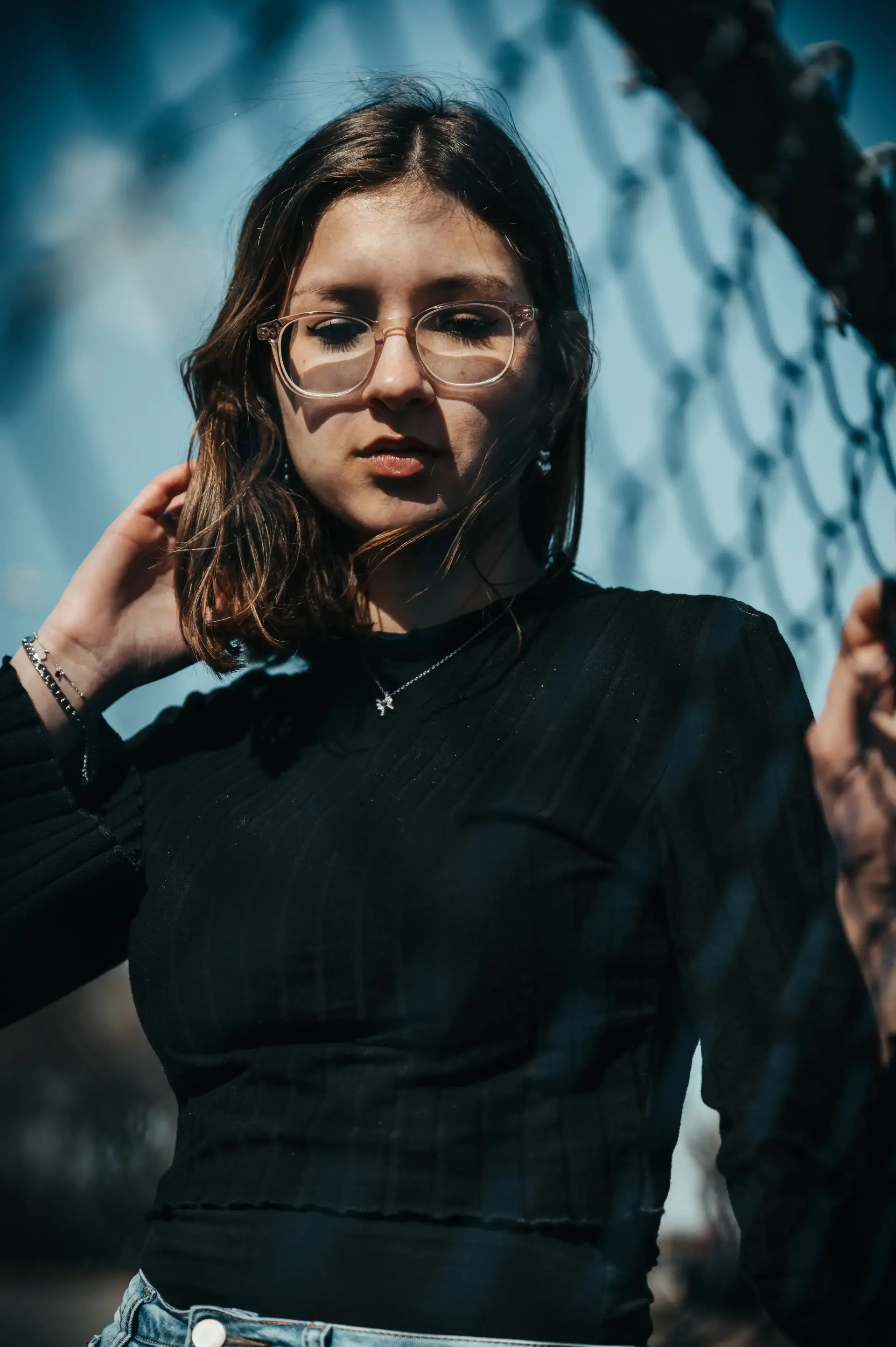 une femme portant des lunettes et un haut noir devant une clôture en maillons de chaîne.